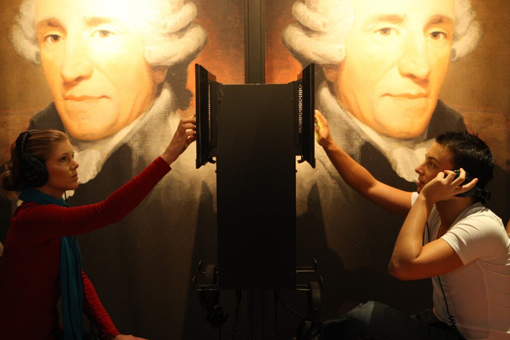 Zwei Besucher:innen hören sich Stücke und Infos zum Komponisten Joseph Haydn an